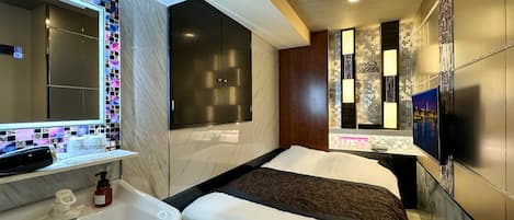 A modern hotel room with a large mirror, a bed with a black headboard, a white sink, and a television mounted on the wall.