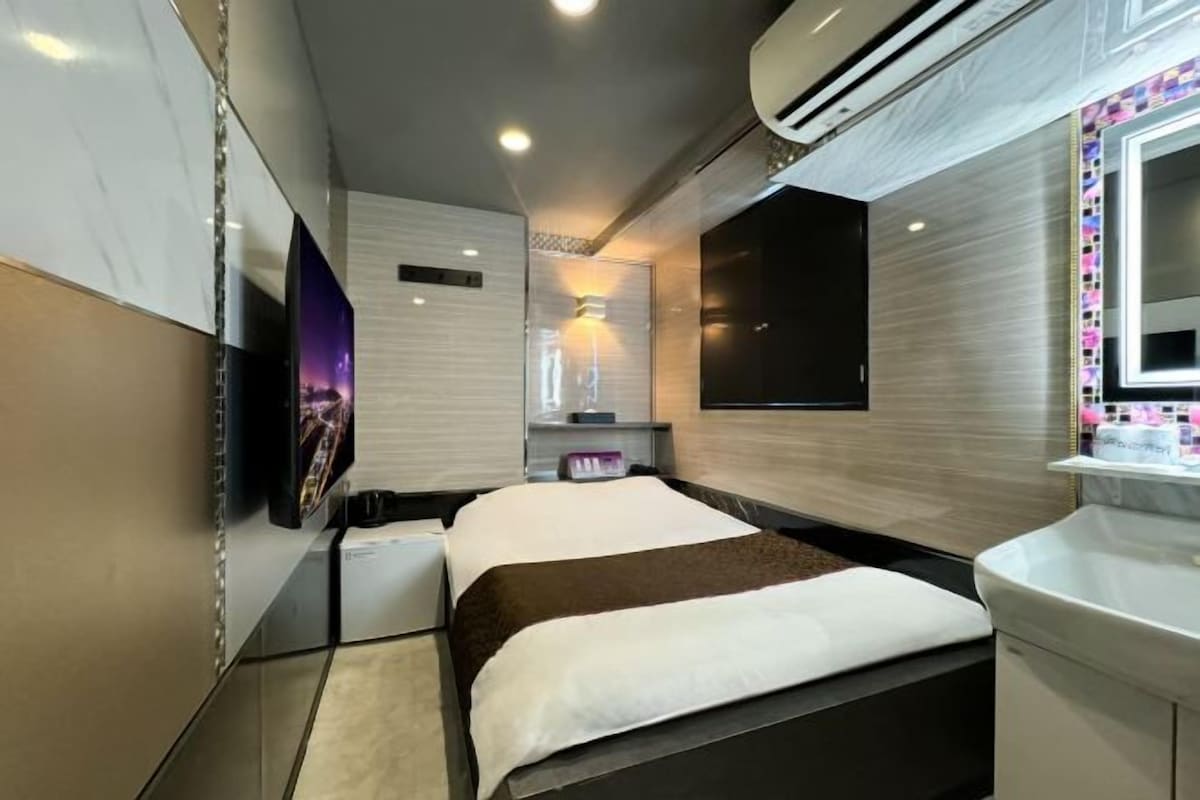 A modern hotel room with a bed, a TV, a desk, and a bathroom.