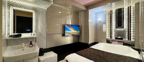 Una habitación de hotel moderna con una cama grande, televisión integrada, tocador con espejo y un refrigerador pequeño.
