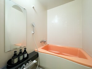 Een badkamer met een groot, oranje bad, een wit wastafeltje met een zwart aanrechtblad en een spiegel boven het wastafeltje.