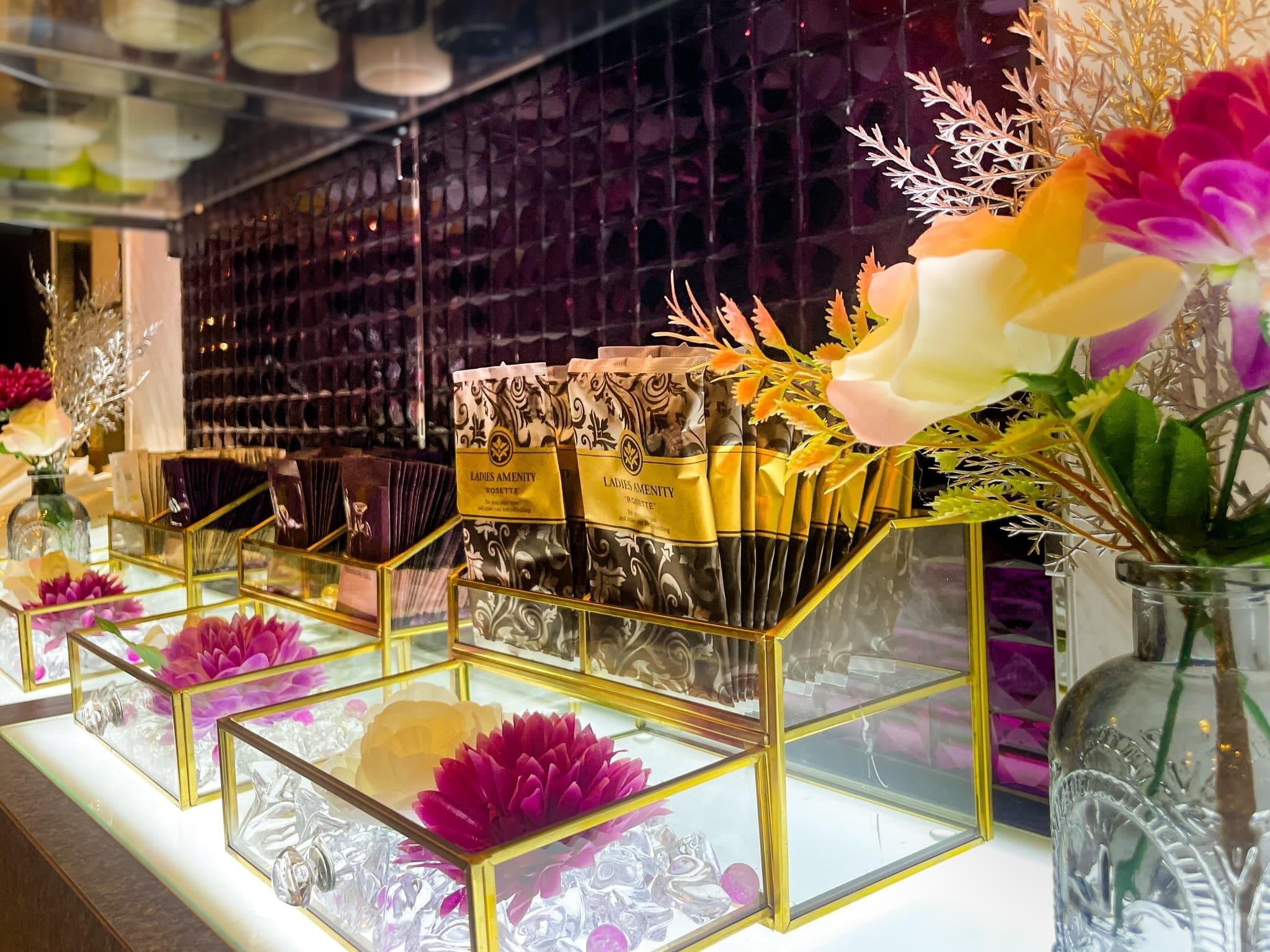 A display of luxury items, including a selection of perfumes and decorative flowers in glass containers.