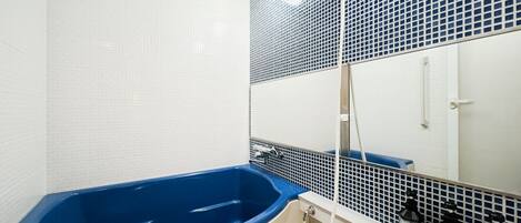 Een badkamer met een blauw bad, witte betegelde wanden en een spiegel met een rasterpatroon.