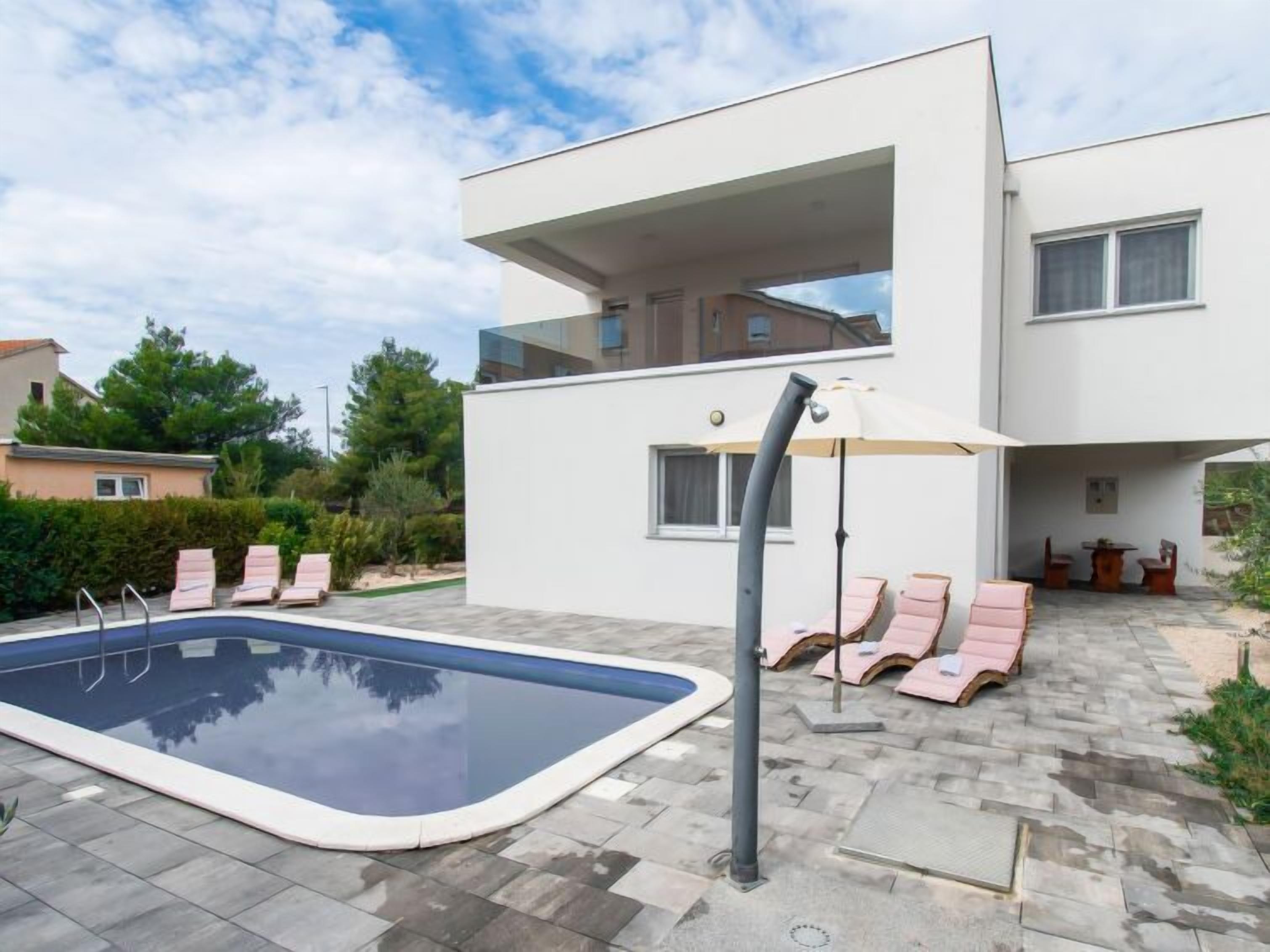 Ein modernes, zweistöckiges Haus mit Swimmingpool, Liegestühlen und einer Terrassenfläche.