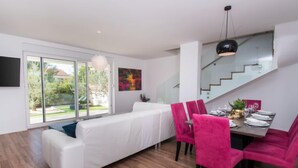 Een moderne woonkamer met een witte bank, een eettafel voor vier personen en een trap naar een hoger gelegen verdieping.