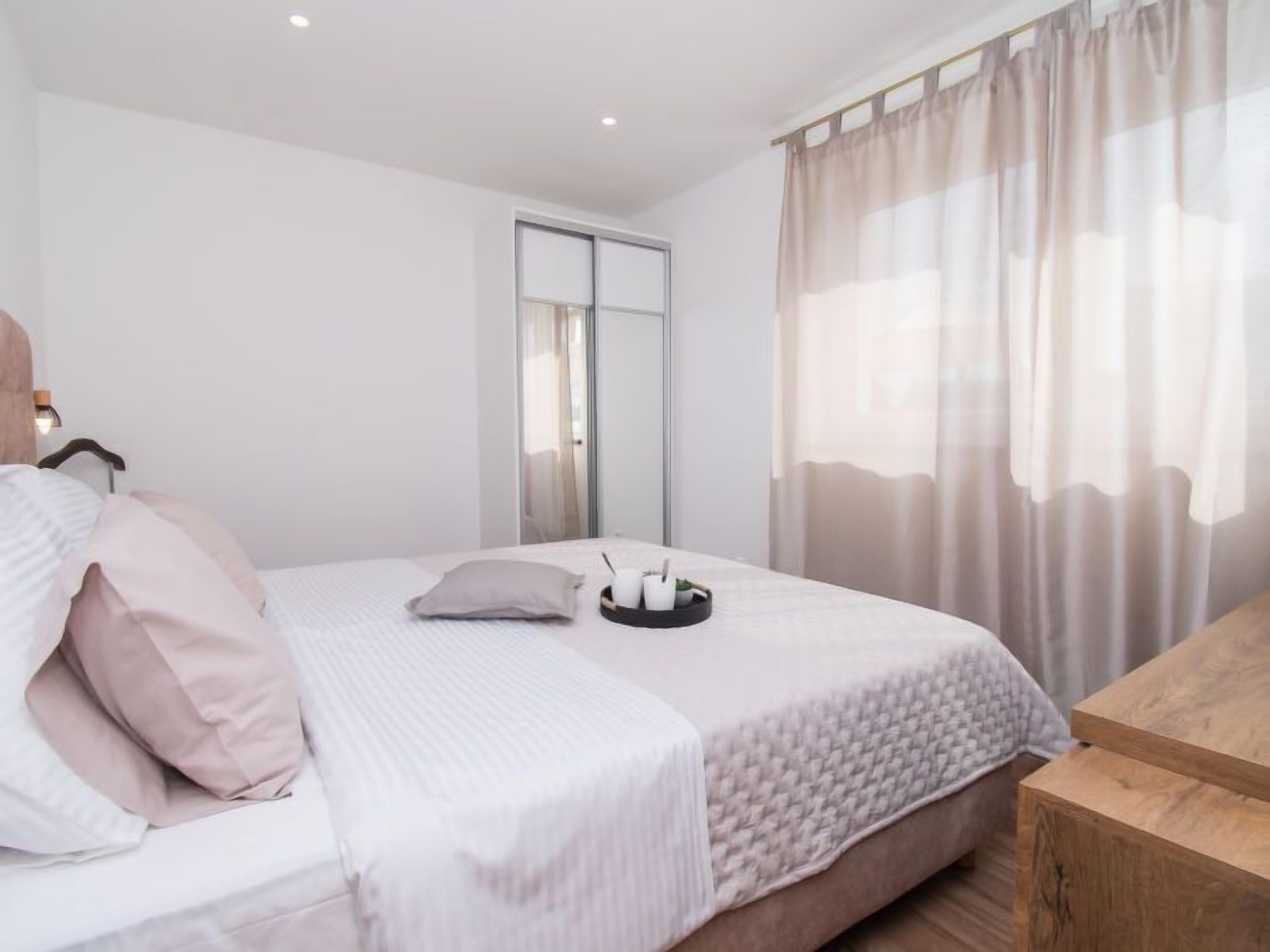 A bedroom with a bed, a bedside table, a mirror, and a window with curtains.
