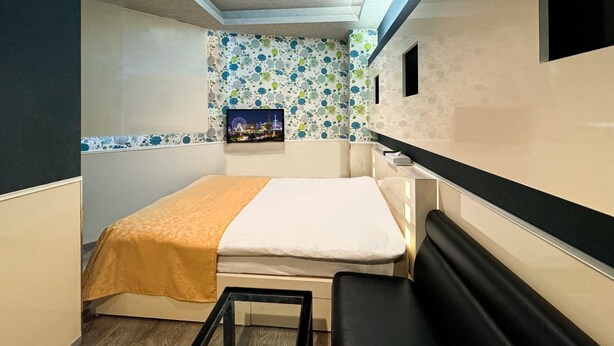Une chambre d’hôtel de taille réduite, comprenant un lit, un petit bureau, un téléviseur fixé au mur et un papier peint à motifs.