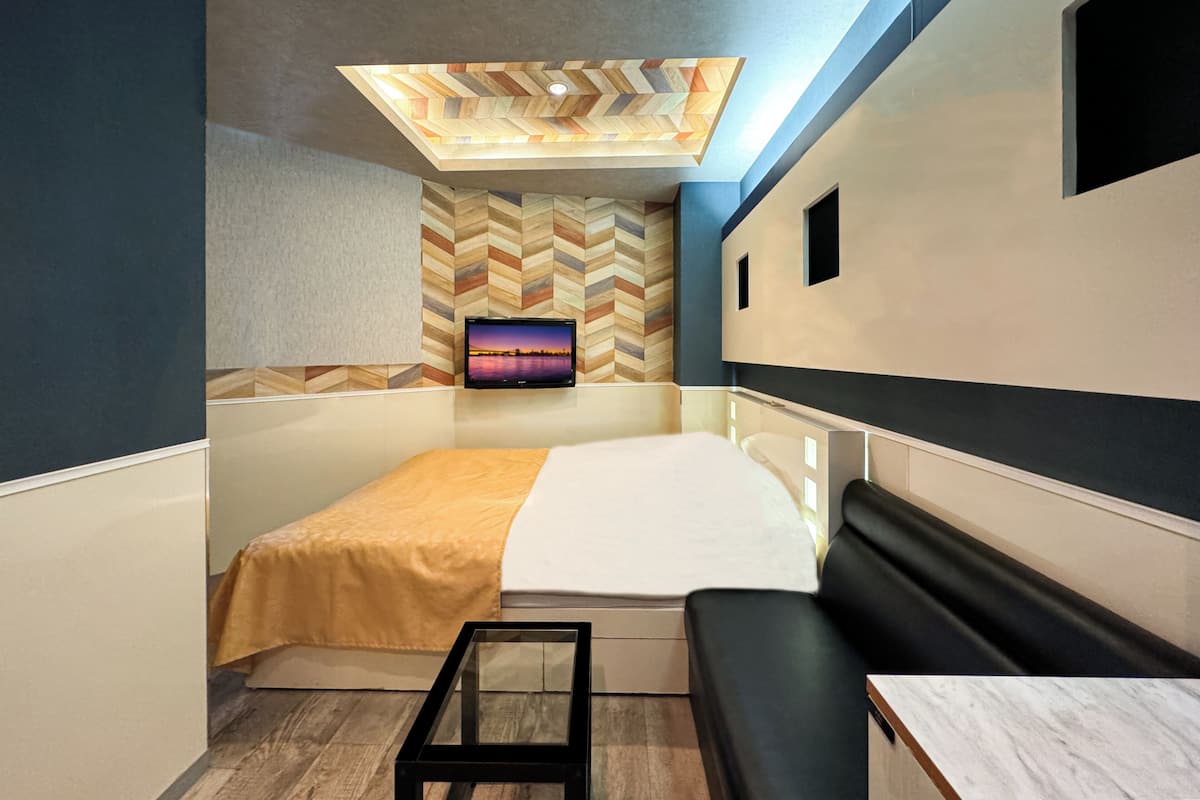 A modern room with a bed, a TV mounted on the wall, a small table, and a bench.