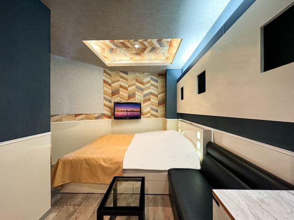 A modern hotel room with a bed, a seating area, a TV mounted on a chevron-patterned wall, and a skylight above.