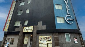 Un hôtel à plusieurs étages, reconnaissable à son grand panneau « Hôtel Century », à ses nombreuses fenêtres et à son entrée bien visible.
