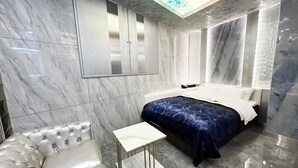 A modern bedroom with a bed, a white sofa, a small table, and a ceiling light fixture. - Hotel Century (Chiba)
