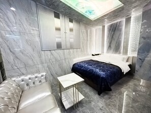 A modern bedroom with a bed, a white sofa, a small table, and a ceiling light fixture. - Hotel Century (Chiba)