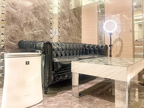 A black leather sofa with a tufted design, a white trash can, and a marble-patterned floor.