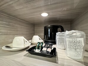 A hotel room with a black coffee maker, white cups, a tray with sugar packets, and a bag of hand sanitizer. - Hotel Century (Chiba)