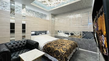 A modern hotel room with a large bed, a black leather sofa, and a small table.