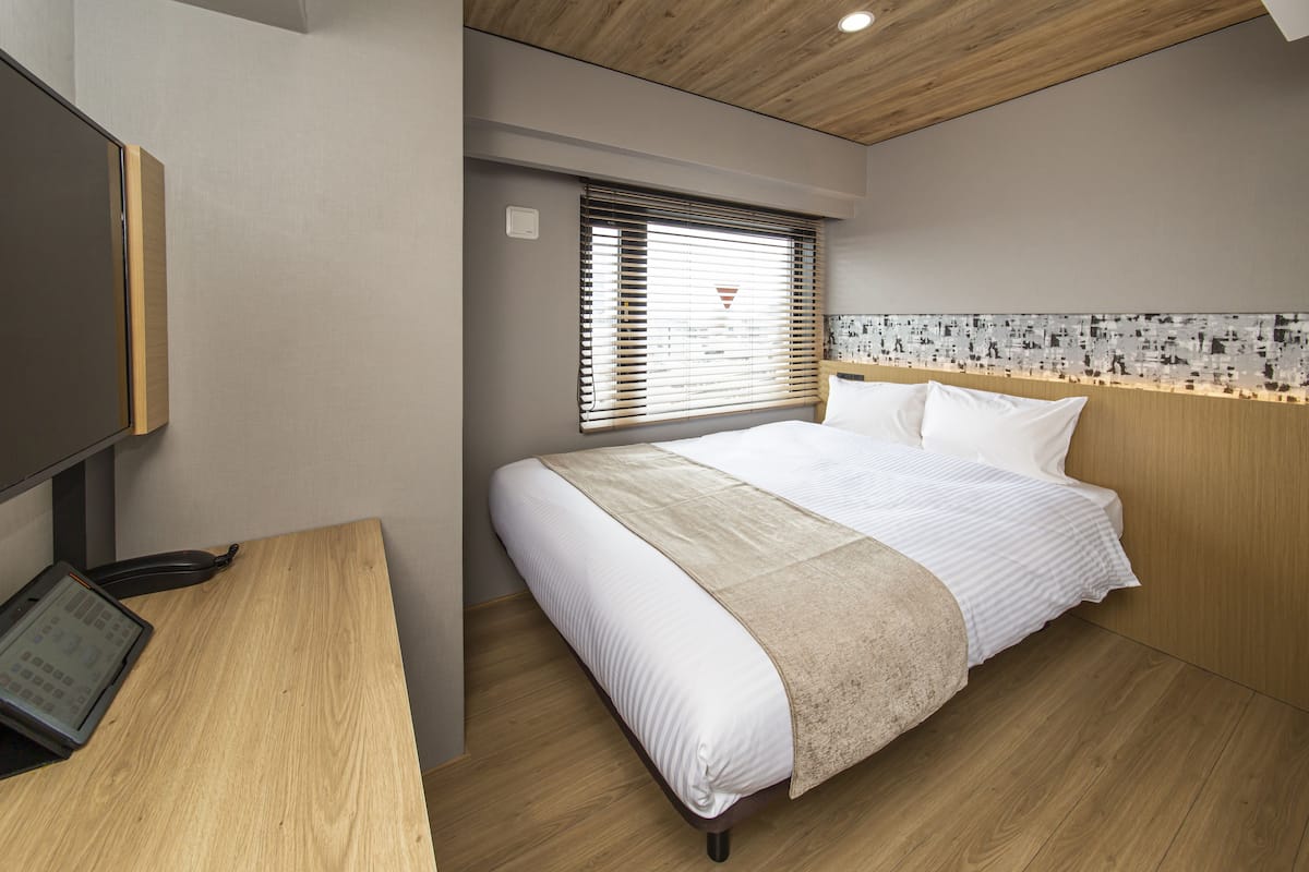 A bedroom with a bed, a desk, and a window with blinds.