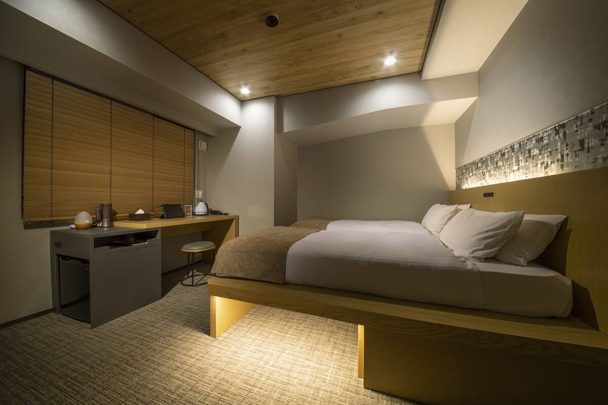A modern bedroom with a wooden bed, a desk, and a small kitchenette.