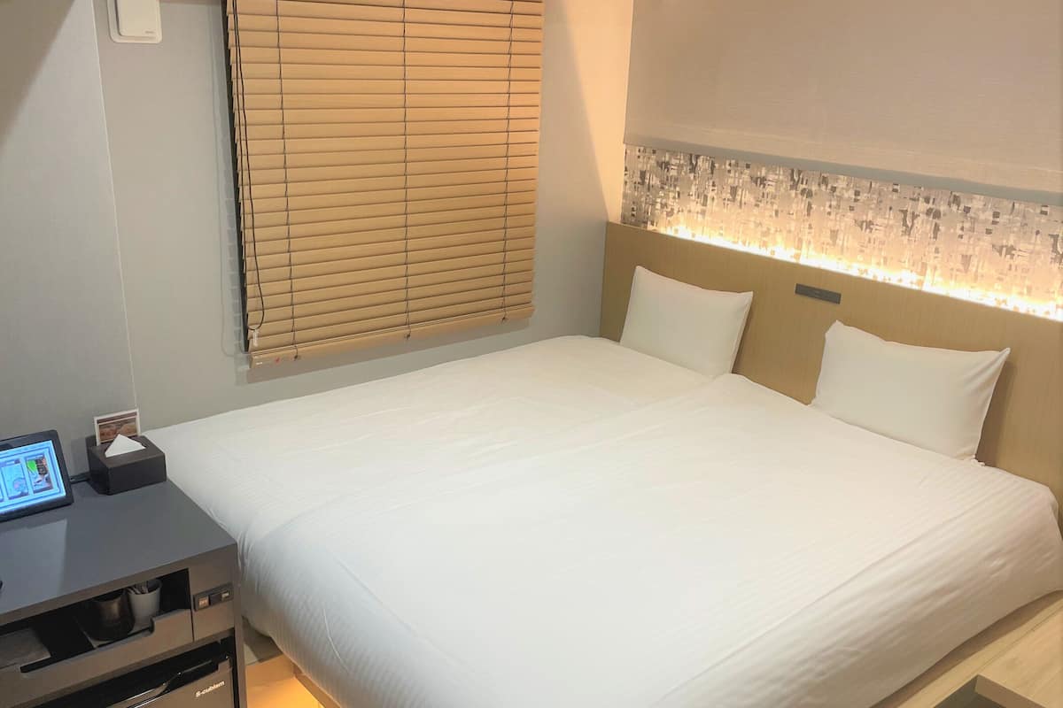 A hotel room with a bed, bedside table, and a control panel.