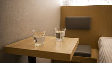 Ein kleiner Holztisch mit zwei Wassergläsern und einem grauen Kopfkissen auf einem Bett in einem Hotelzimmer.