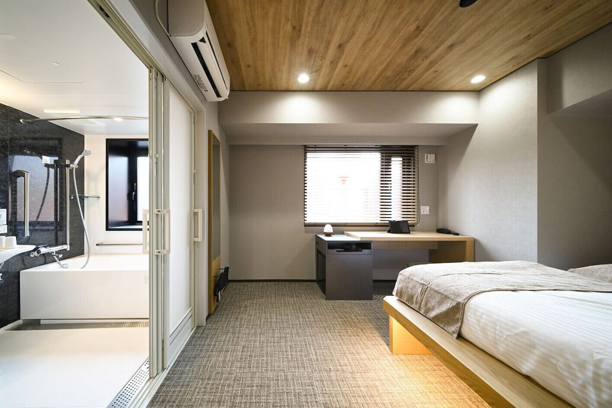 A modern hotel room with a bed, desk, and shower area.