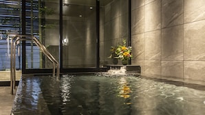 Una piscina interior moderna con agua cristalina, una escalera metálica y un jarrón con flores.