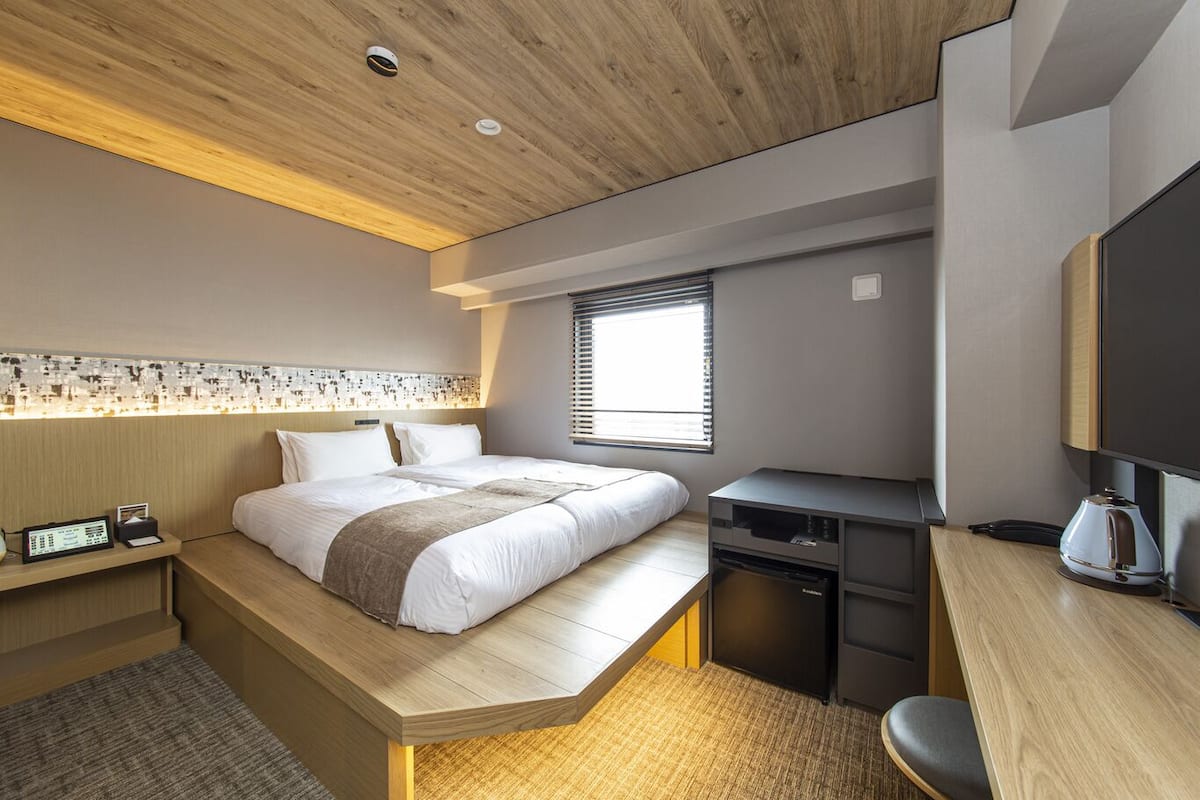 A modern hotel room with a bed, desk, and built-in TV.