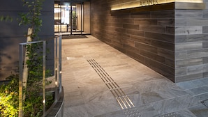 Exterior del Hotel Amanek con un diseño moderno, que destaca un cartel iluminado, un techo de madera y una fachada de piedra.
