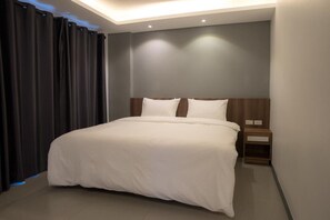 A modern hotel room with a large bed, dark curtains, and a wooden headboard. - The Zleep Chonburi (Chonburi)