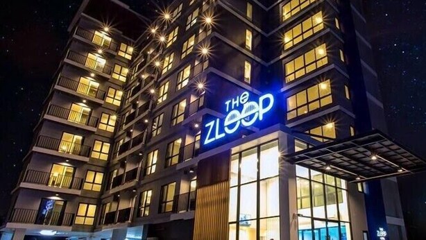 Un bâtiment moderne à plusieurs étages, doté d’une enseigne lumineuse bien visible sur laquelle on peut lire « The ZLOOP », et d’un hall d’entrée en verre.