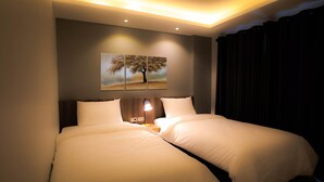 Une chambre d’hôtel avec un grand lit, une table de chevet, une lampe et un tableau représentant un arbre accroché au mur.