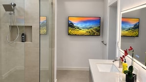 Une salle de bain moderne avec une douche à l’italienne en verre, un grand miroir et deux tableaux représentant des paysages accrochés au mur.
