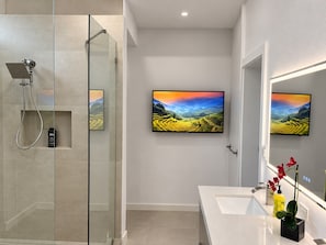Un baño moderno con cabina de ducha de vidrio, un espejo grande y dos cuadros de paisajes en la pared.