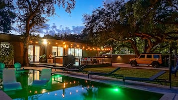 Una piscina con sillas de descanso, un espacio de estar techado al aire libre y un vehículo estacionado cerca.