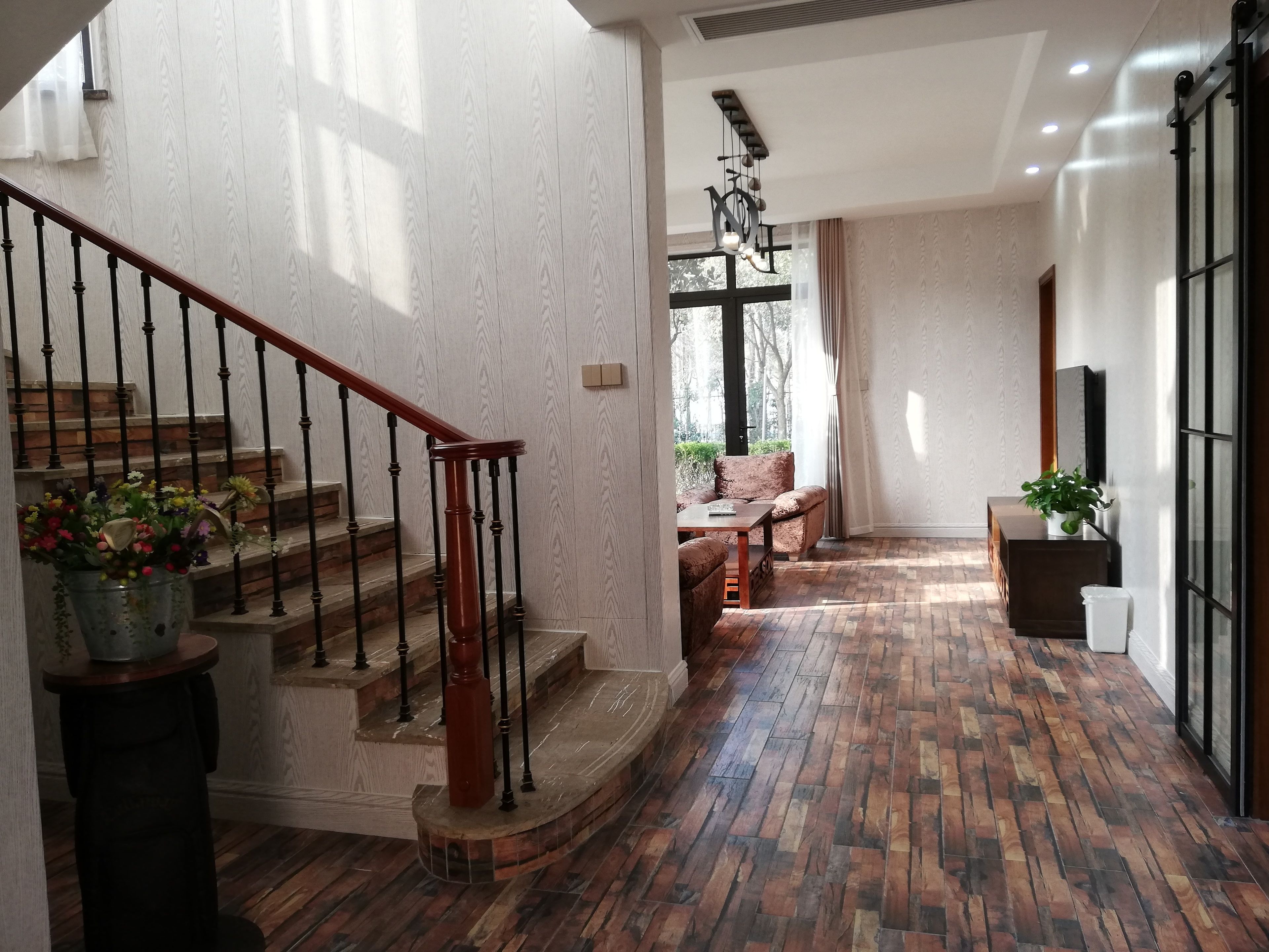 A staircase with a wooden handrail and black balusters, leading to a room with a patterned wall and a large window.