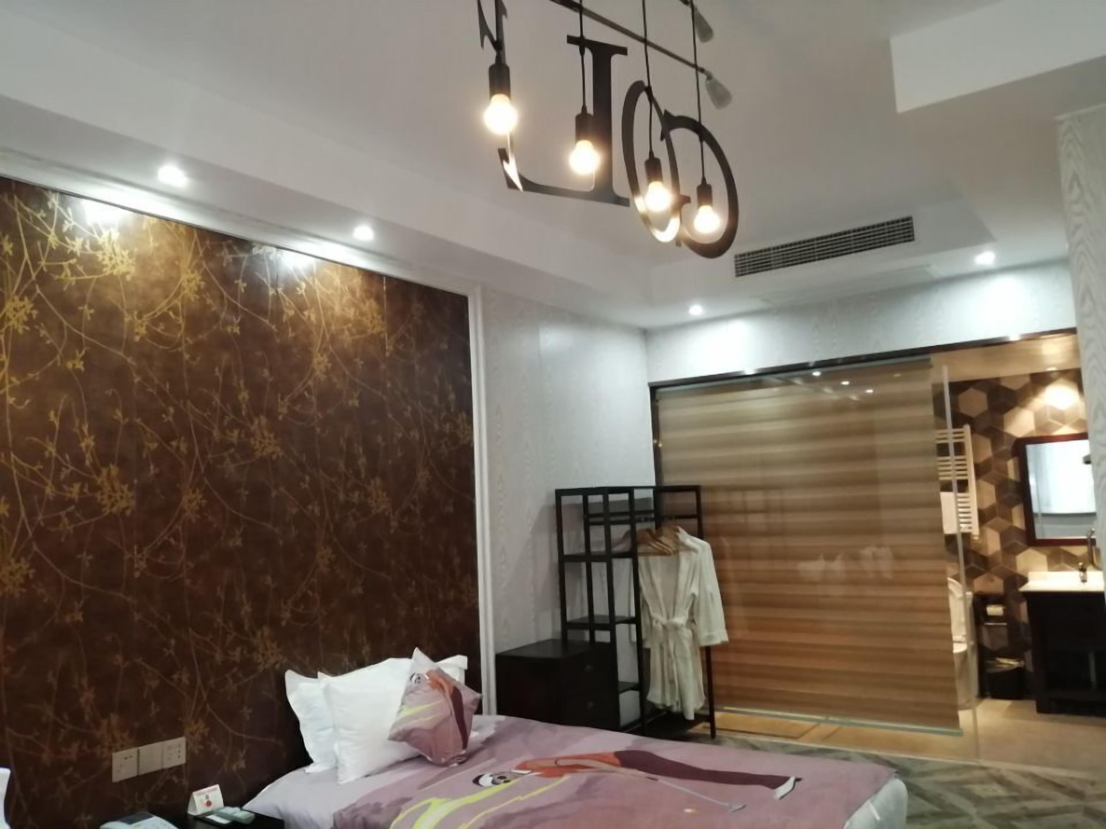 A modern hotel room with a bed, a robe, a wardrobe, and a bathroom visible through a sliding door.