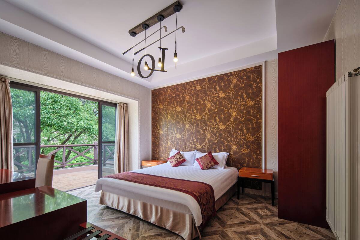 Ein modernes Hotelzimmer mit einem großen Bett, einem Schreibtisch und einem Balkon mit Blick auf Bäume.