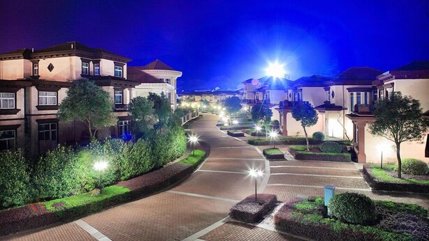 A residential street at night with houses on both sides, illuminated streetlights, and a clear sky.