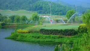 A golf course with a pond, surrounded by lush greenery and hills.