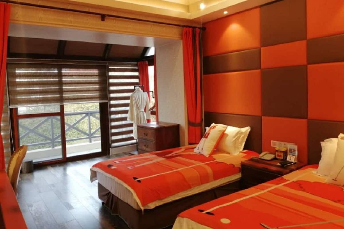 Ein Hotelzimmer mit zwei Betten, einem Holz-Kopfteil, einem Fenster mit Jalousien, einer Holzkommode und Blick auf einen Balkon.