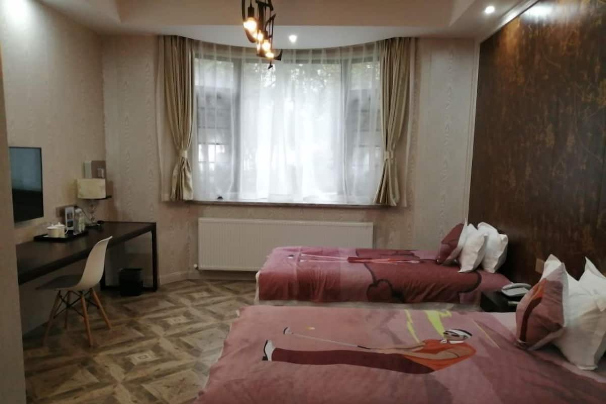 Ein Hotelzimmer mit zwei Betten, einem Schreibtisch, einem Stuhl, einem Fernseher und einem Vorhangfenster.