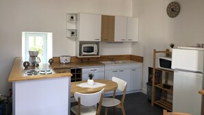 A compact kitchen with white cabinets, a microwave, a toaster, and a sink. There is a small dining table with two chairs and a potted plant. - APARTMENT 1.5 kms FROM THE LANDING BEACHES  (Tracy sur Mer)
