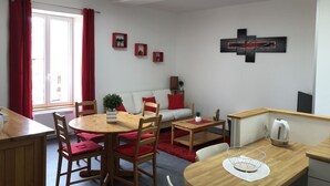 A modern living room with a dining area, featuring a sofa, red cushions, a coffee table, and a wall-mounted artwork. - APARTMENT 1.5 kms FROM THE LANDING BEACHES  (Tracy sur Mer)
