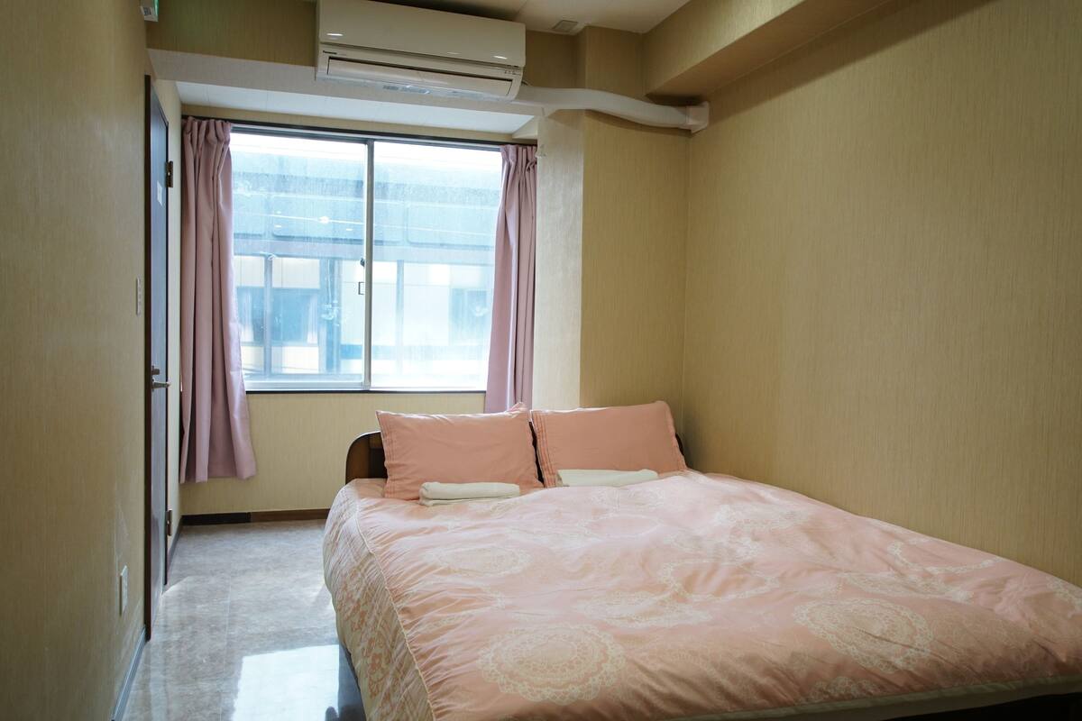 A bedroom with a bed, a window with curtains, and an air conditioning unit.