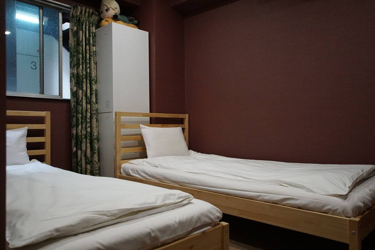 A room with two wooden beds, a white wardrobe, and a window with a curtain.