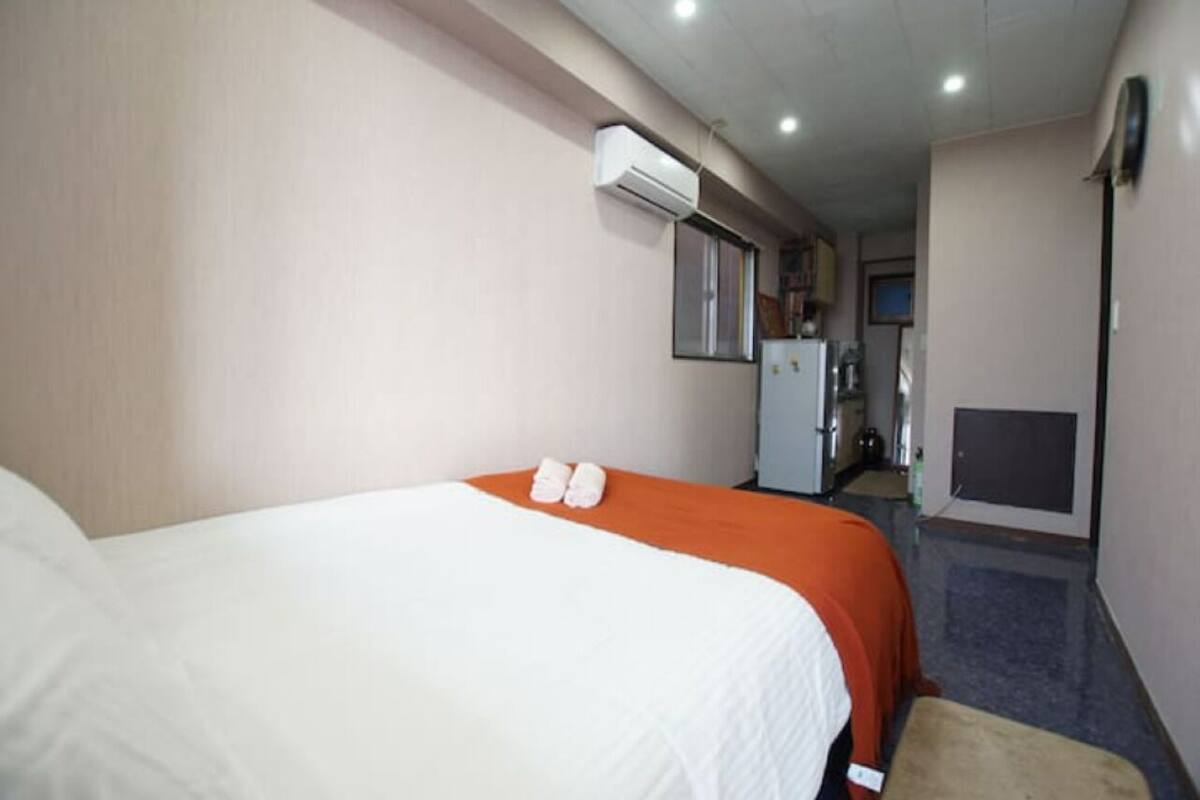 A hotel room with a bed, an air conditioning unit, a small kitchenette, and a television.