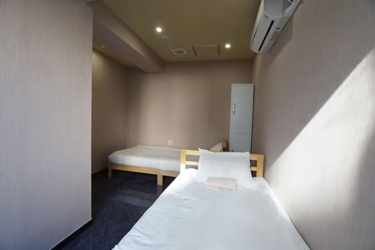 A small, single-bed room with a wooden bed, a wardrobe, and a carpeted floor.