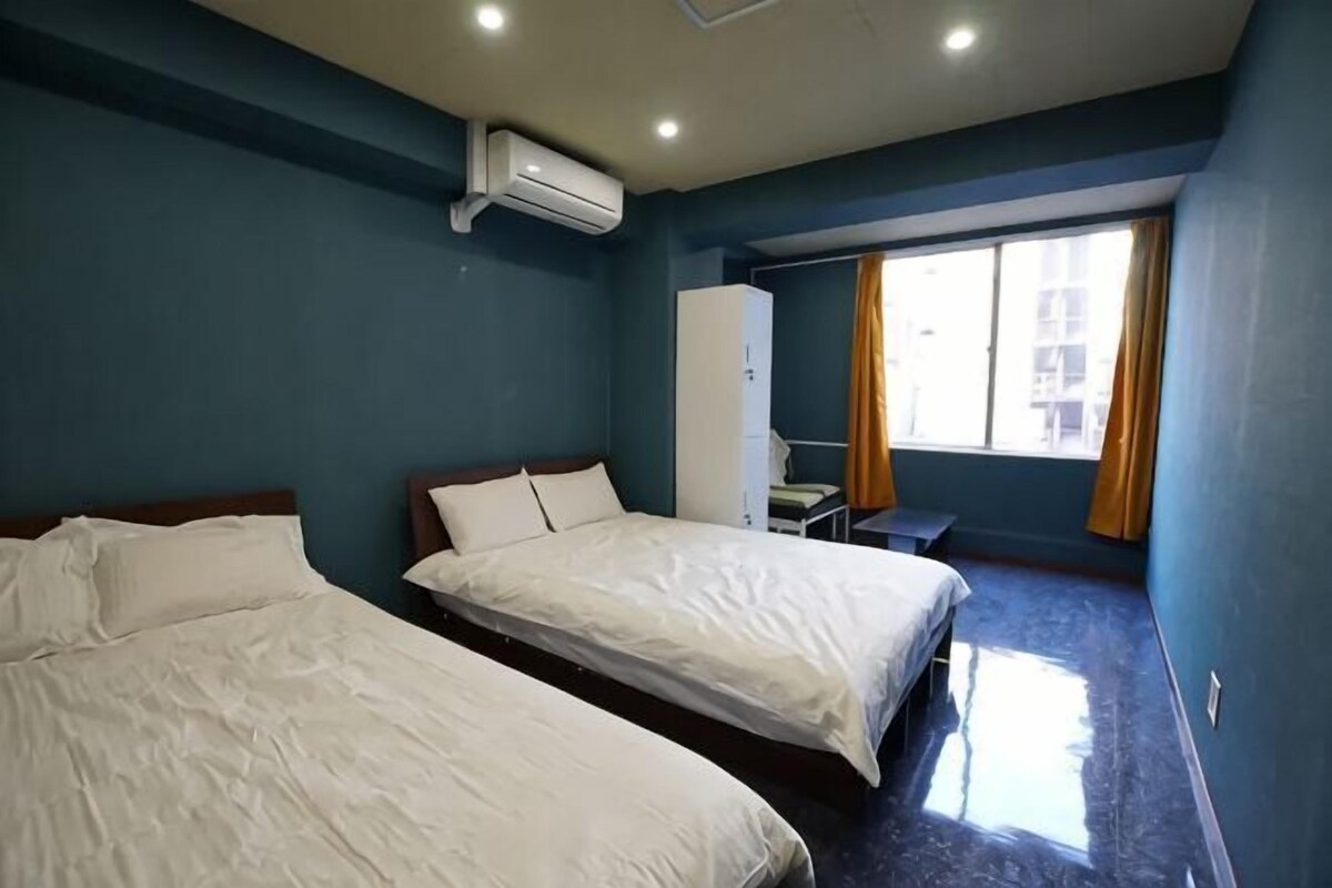 A hotel room with two beds, a desk, a chair, a wardrobe, and a window with curtains.