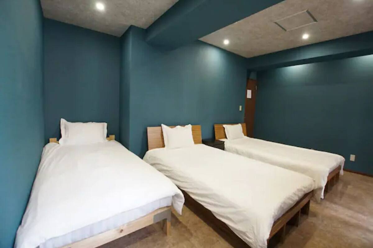 A room with three single beds, wooden headboards, and a blue wall.