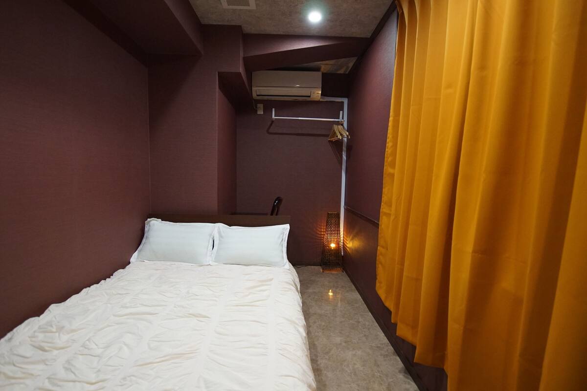 A hotel room with a bed, a wardrobe, an air conditioning unit, and a curtain.
