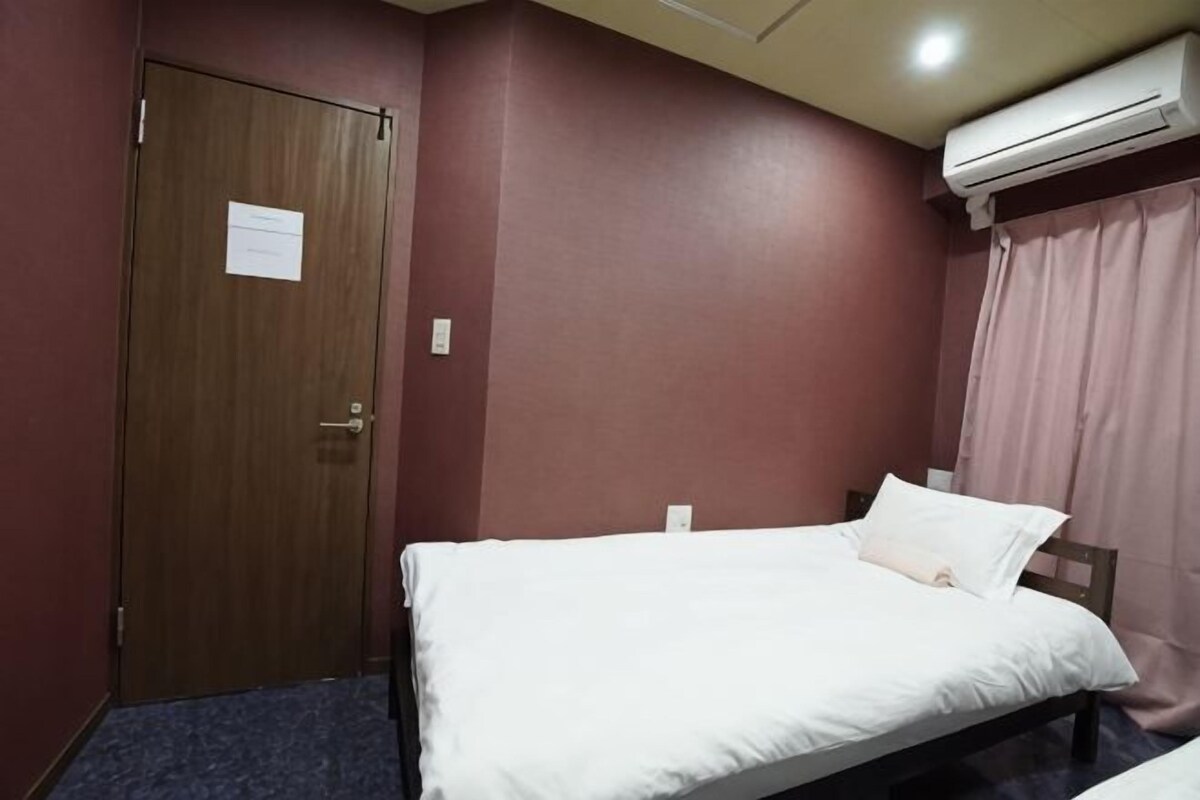 A hotel room with a single bed, a wooden door, and an air conditioning unit.