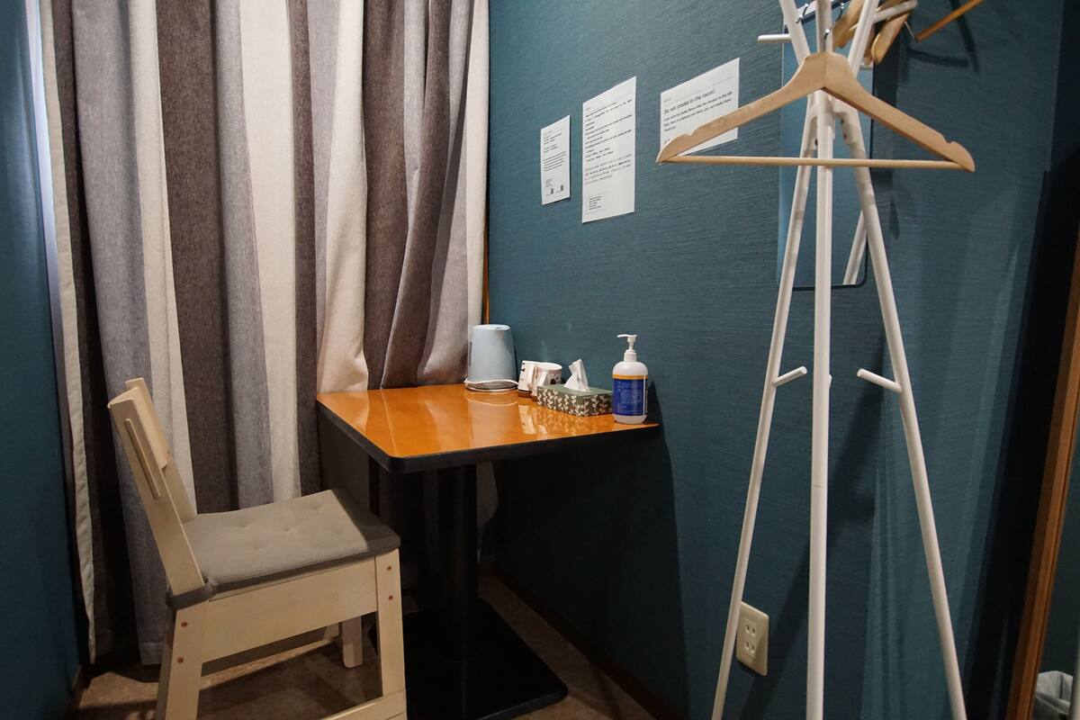 A small room with a wooden chair, a table with a tissue box, a bottle, and a hanger.